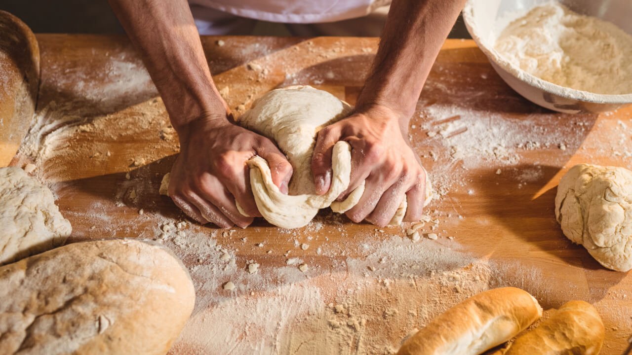 A Baker kneading Bread Dough with Flour