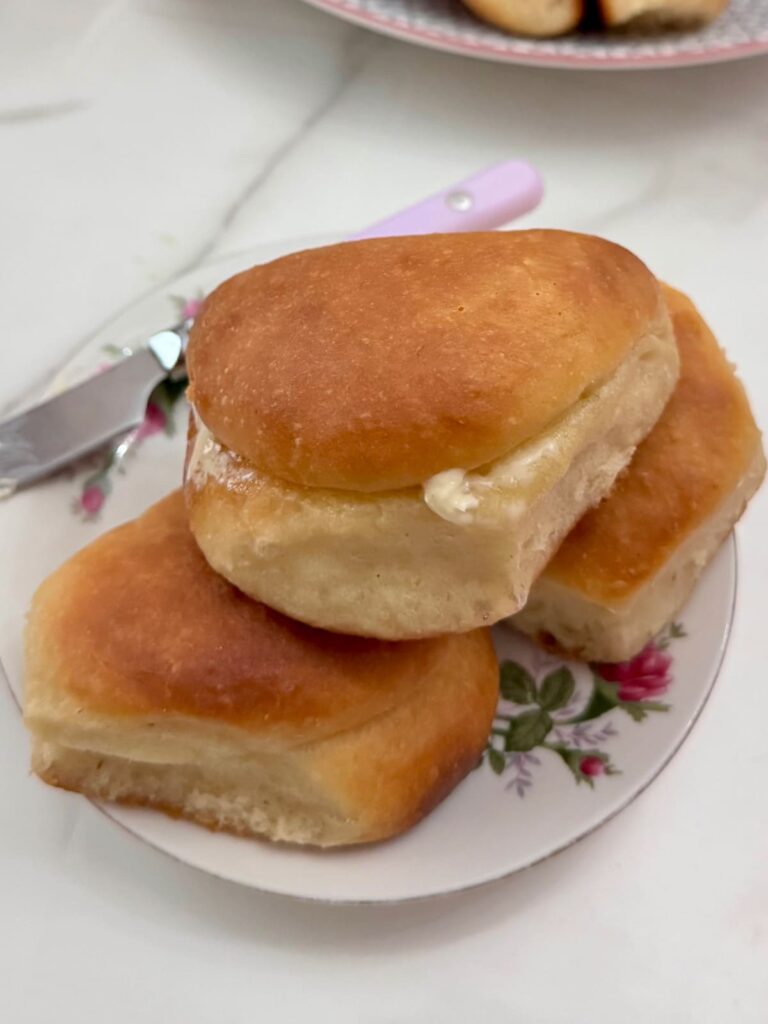 3 Parker House rolls on a small plate with a knife.
