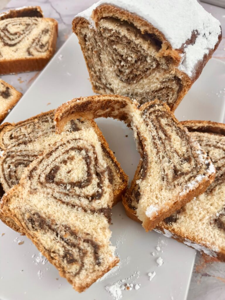 A partially sliced loaf and broken pieces of povitica on a white tray.
