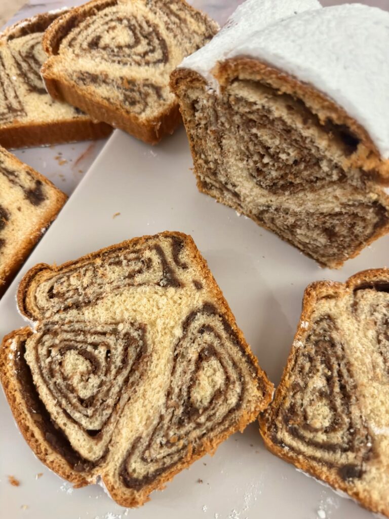 Slices of Povitica walnut swirl bread with powdered sugar on a white plate.