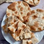 Stacked rounds and broken pieces of communion bread on a white plate.