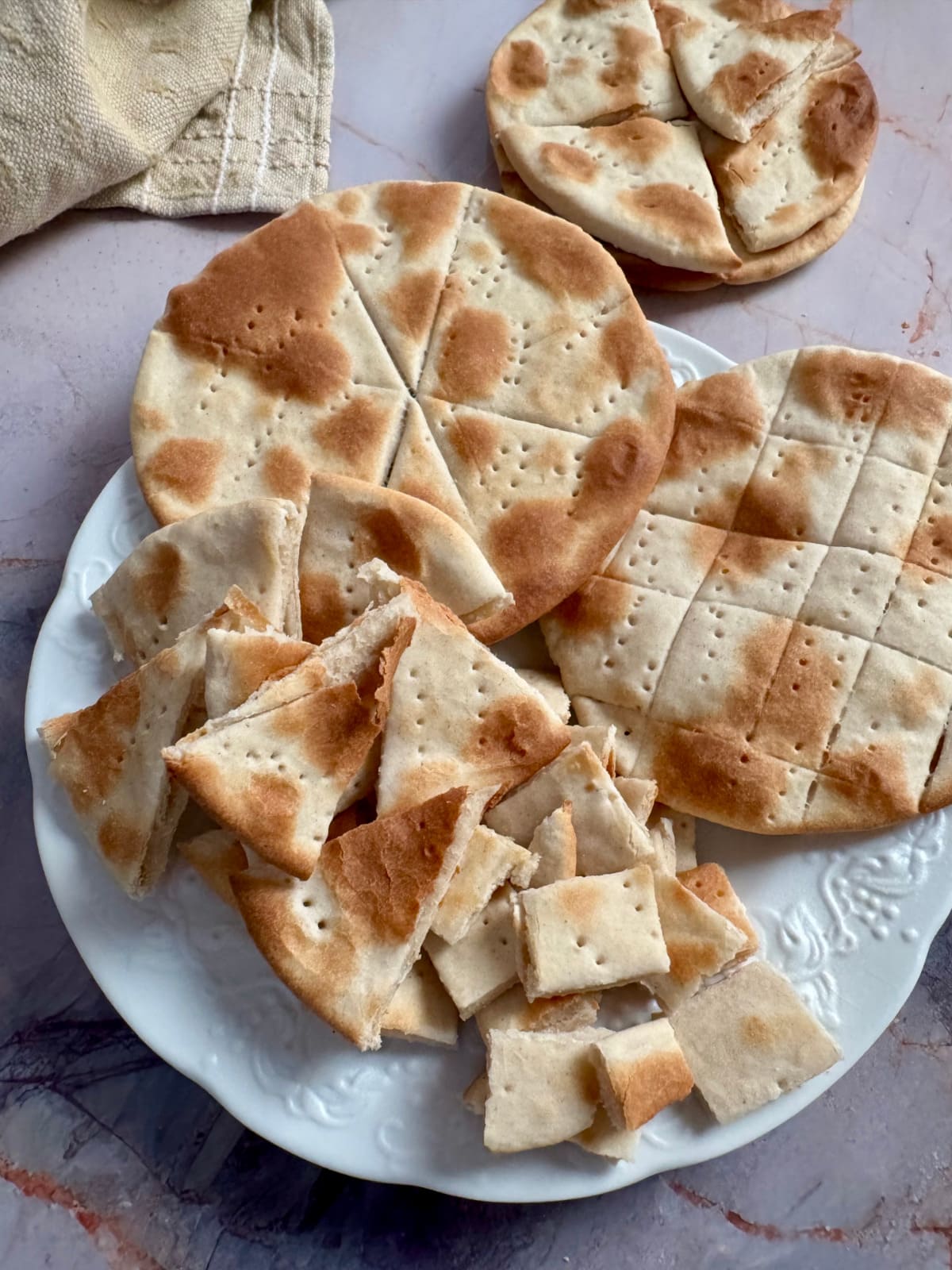 Stacked rounds and broken pieces of communion bread on a white plate.