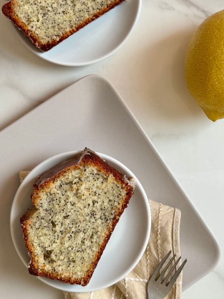 Two slices of iced lemon poppy seed bread on a white plate.
