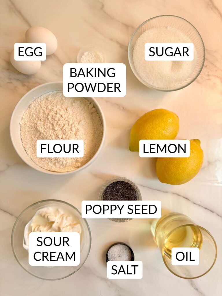 An overhead view of the ingredients used for lemon poppy seed bread, including flour, sugar, eggs, lemons, oil, sour cream, poppy seeds, baking powder, and salt.
