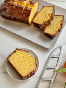 A single slice of iced orange bread on a small plate next to a silver knife and the rest of the loaf.