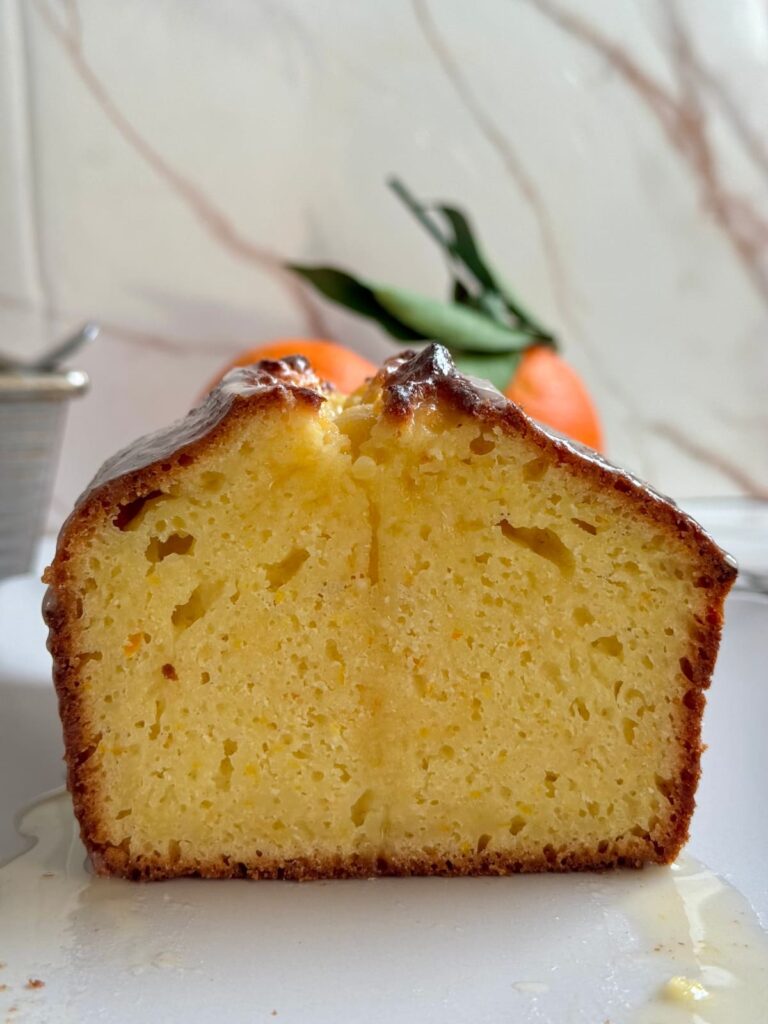 A close-up view of the dense, yellow interior of a sliced orange bread loaf, with icing dripping down the sides.