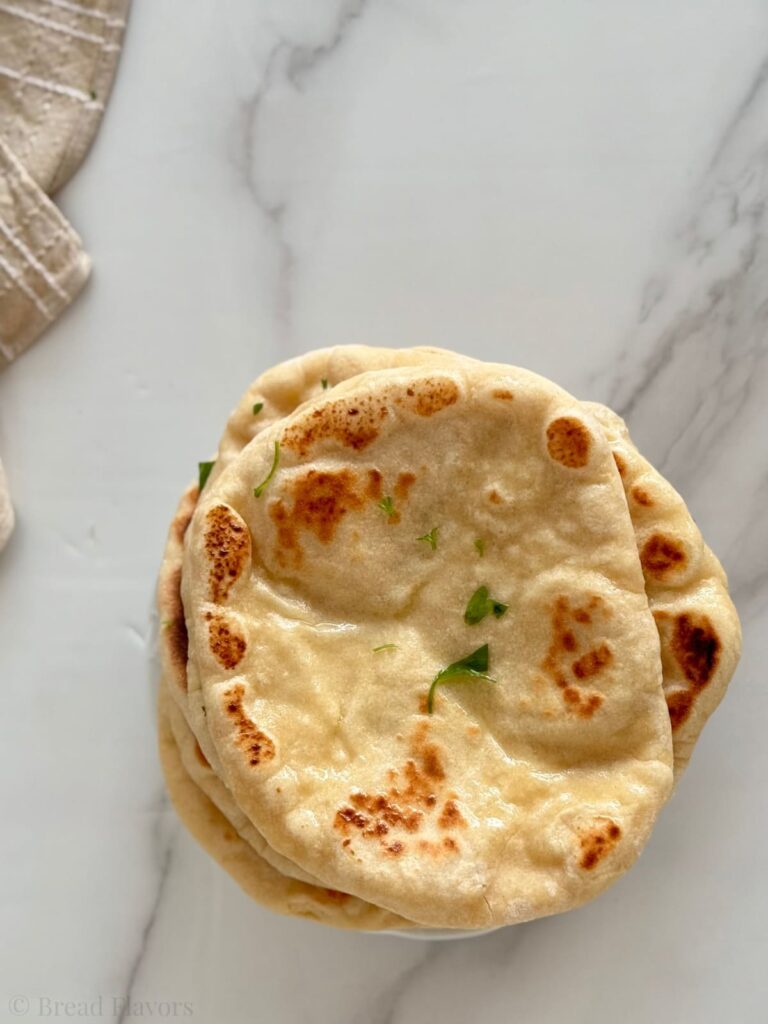 Top-down view of a stack of fluffy, golden-brown 2 ingredient naan breads garnished with fresh parsley.