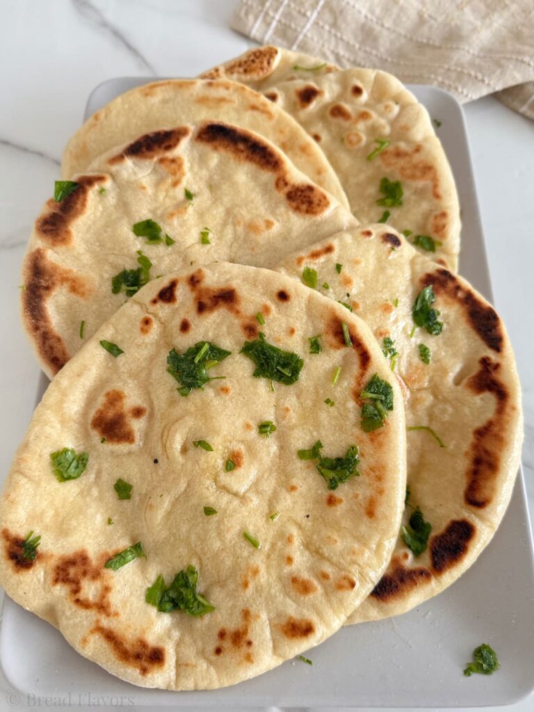 A pile of freshly cooked 3 ingredient naan breads with visible air bubbles and parsley garnish.