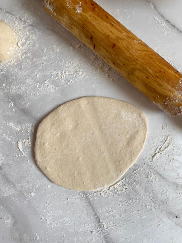 Rolled out piece of dough next to wooden rolling pin on a floured counter.