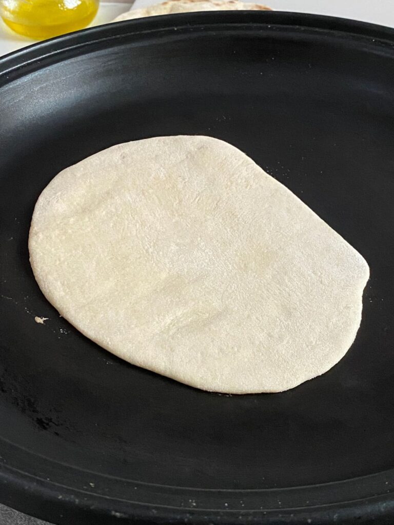 A piece of rolled-out naan dough beginning to cook in a  skillet.