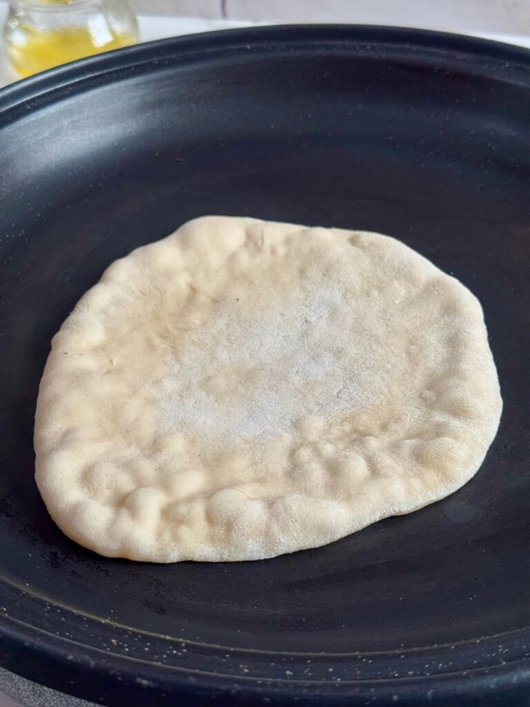 2 ingredient naan dough cooking in a pan, showing small bubbles forming on the surface.