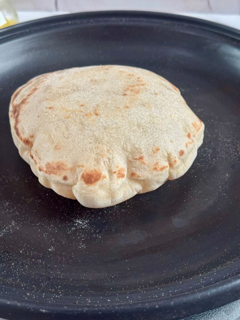 A piece of 2 ingredient naan bread puffing up significantly in a hot skillet, developing golden-brown toasted spots.
