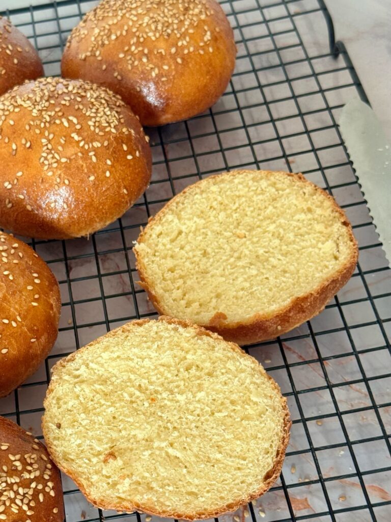 A semolina bun sliced in half on a wire rack, revealing a soft, airy, pale-yellow interior crumb.