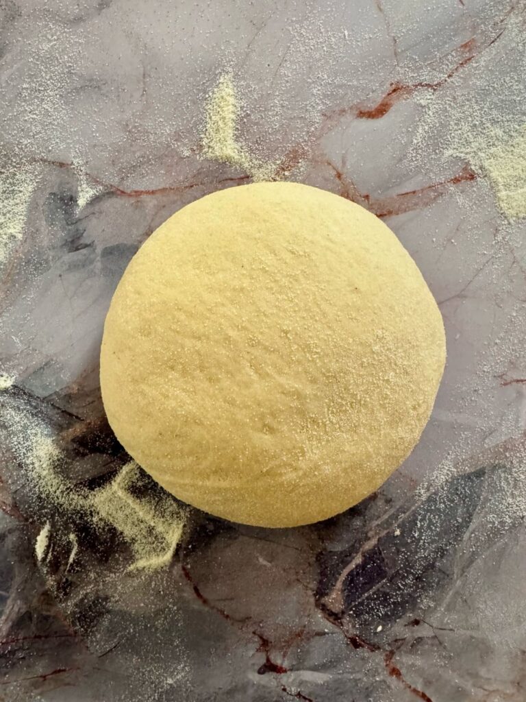 smooth round of semolina dough resting on a floured marble surface.