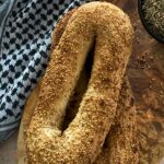 wo sesame-crusted Jerusalem bagels stacked on a wooden board next to a keffiyeh.