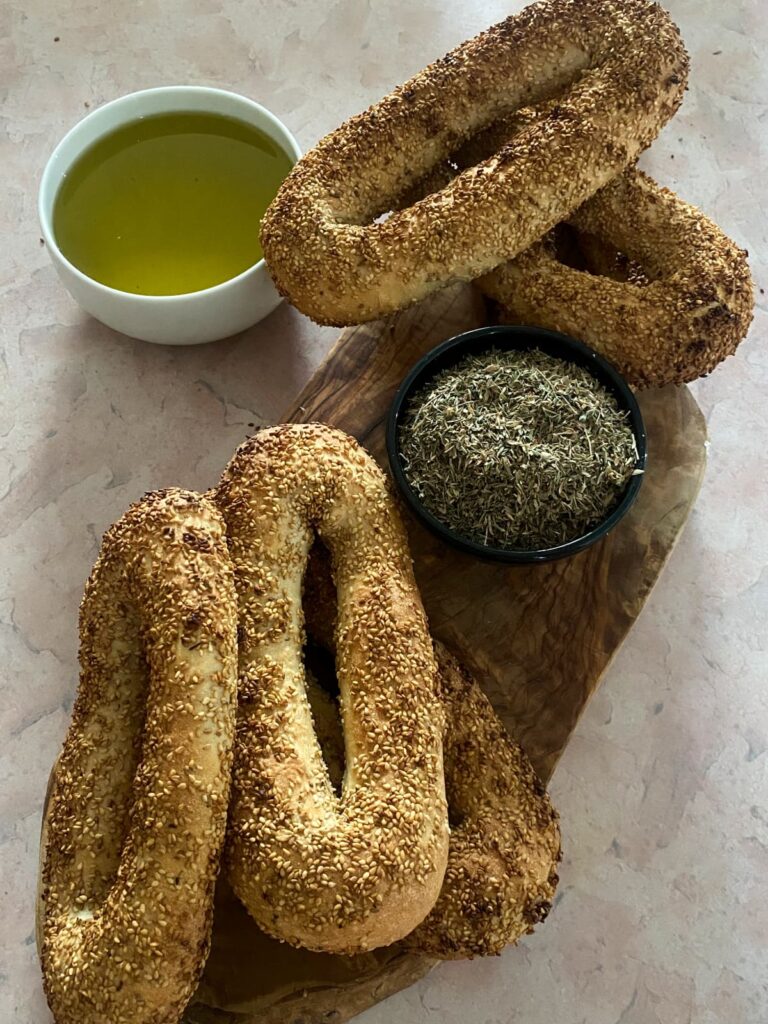 Jerusalem bagels on a wooden board with a bowl of olive oil and a bowl of za'atar.