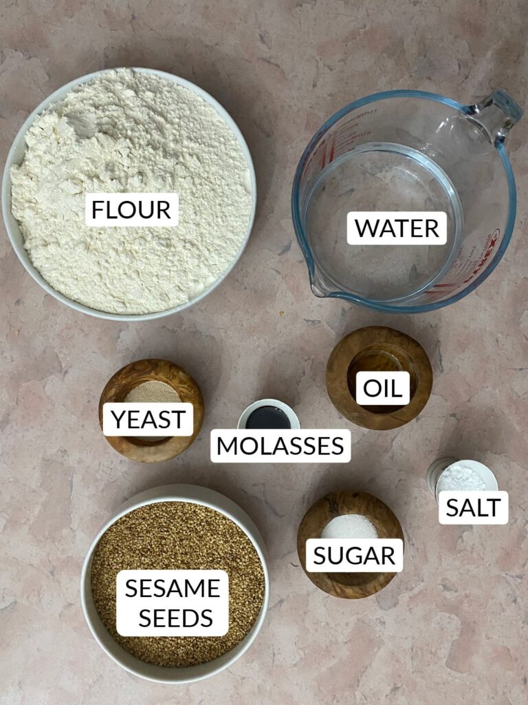 An overhead view of Jerusalem bagels ingredients: flour, water, yeast, molasses, oil, salt, sugar, and a large bowl of sesame seeds.