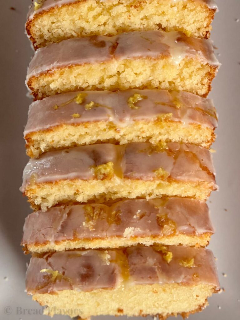 A top-down, close-up view of a glazed lemon loaf cut into thick, even slices.
