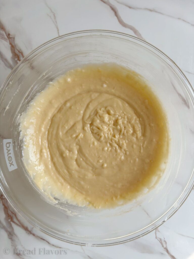A top-down view of thick, creamy lemon bread batter in a clear glass mixing bowl.