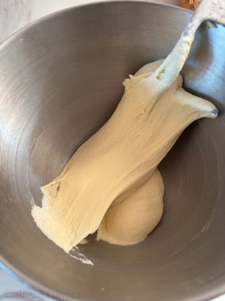 Smooth, elastic semolina roll dough in a stainless steel mixing bowl.