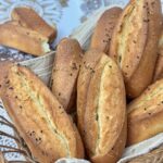 A warm, close-up shot of golden semolina rolls in a basket, highlighting the scoring and seed garnish.
