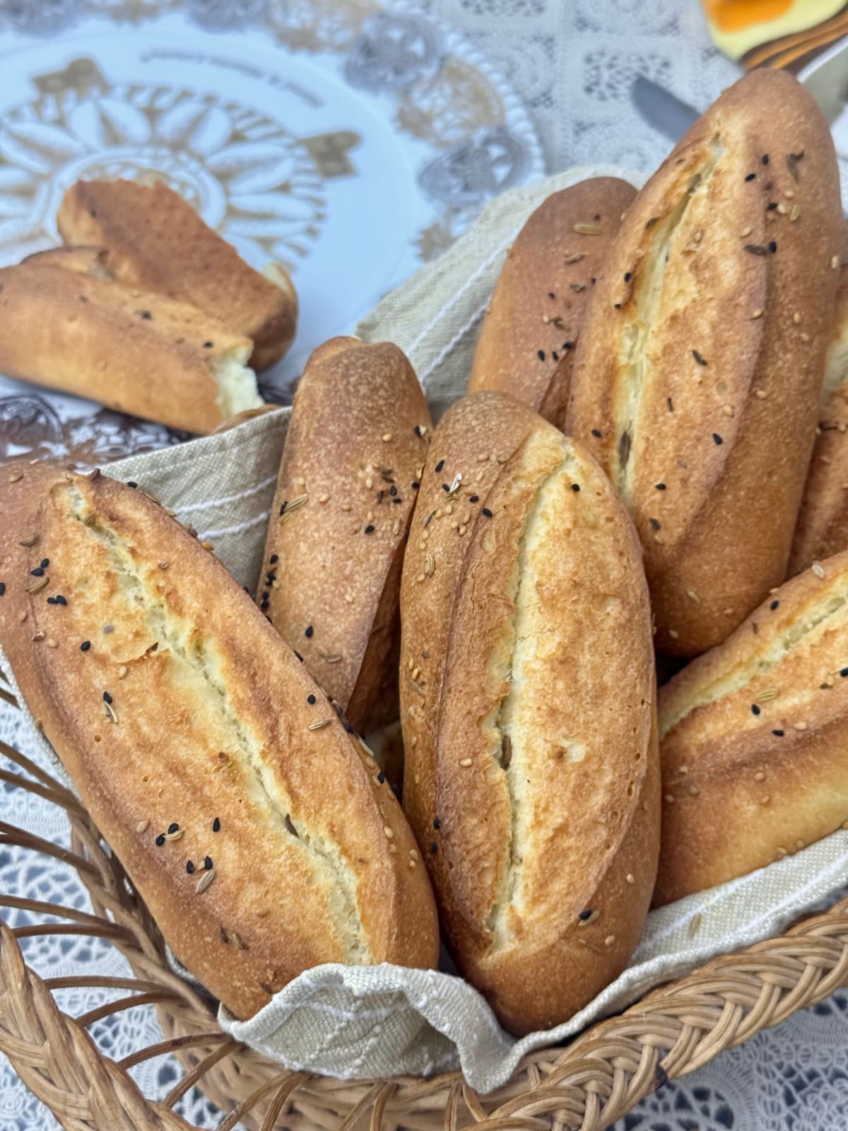 A warm, close-up shot of golden semolina rolls in a basket, highlighting the scoring and seed garnish.