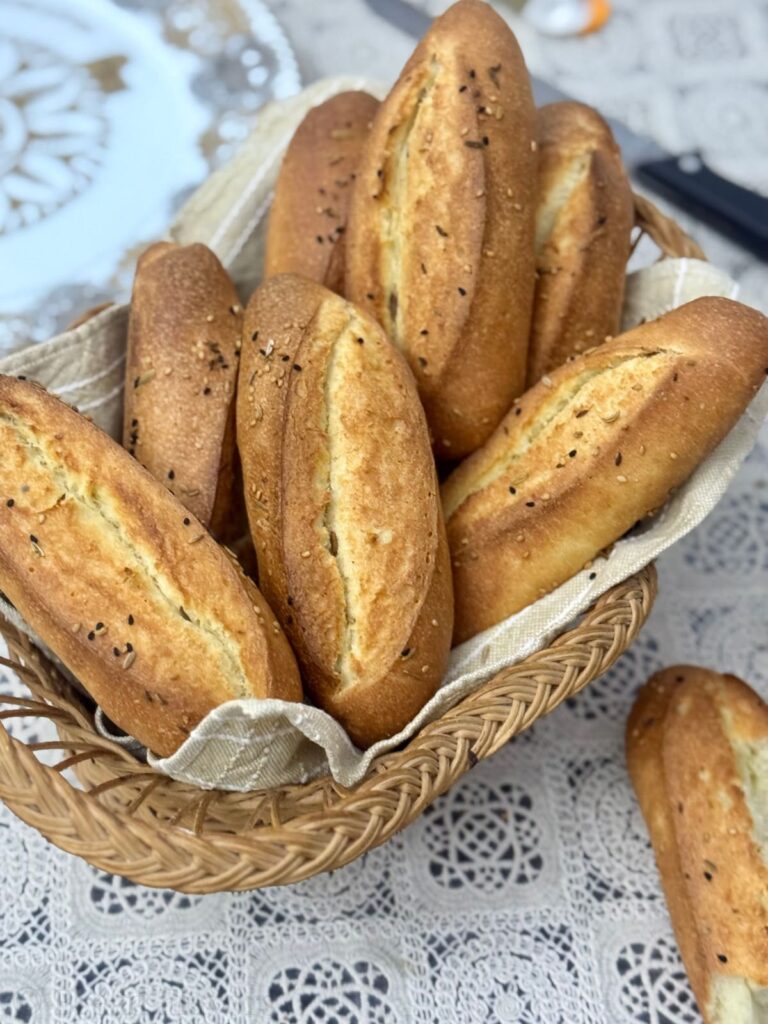 A cluster of golden-brown semolina rolls, featuring a crisp, scored crust and a sprinkle of seeds, resting on basket.

